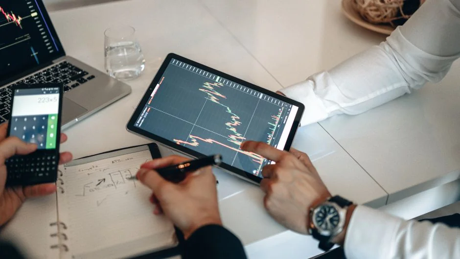 Team examining financial charts and digital data on tablets in an office setting.